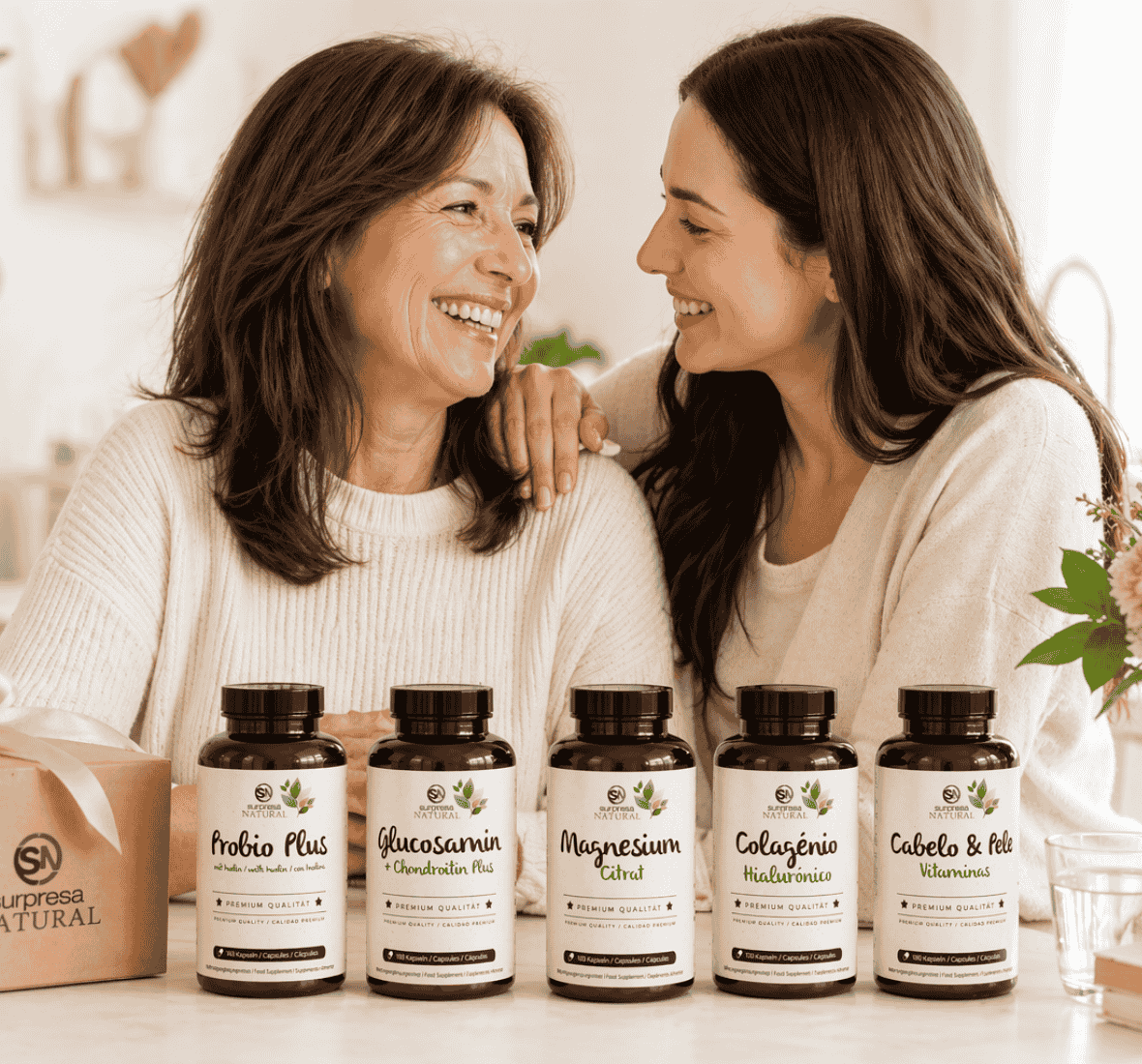 Mãe e filha sorridentes numa cozinha luminosa com uma caixa presente e suplementos Surpresa Natural alinhados sobre a mesa